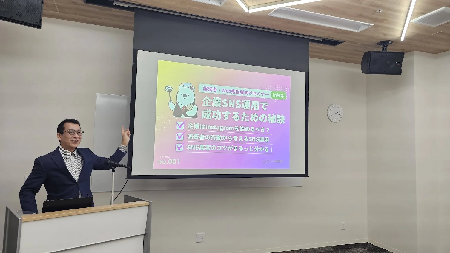 セミナー会場でスクリーンを指しながら話す講師の岩永